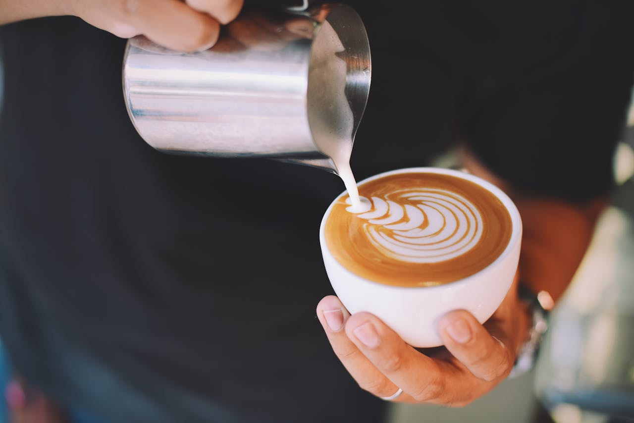 gallery-04 Captivating image of a barista pouring milk art into a cappuccino cup, showcasing latte art skills.
